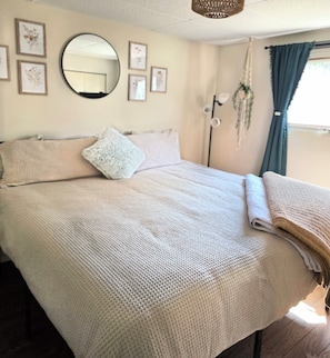 Ein ordentlich bezogenes Bett mit einer gemusterten Decke, einem runden Spiegel und gerahmten Blumenbildern an der Wand.