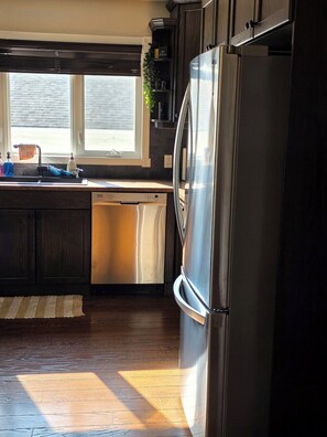 A kitchen with a stainless steel refrigerator, a dishwasher, and a window providing natural light. - ○Small Town Pearl○ 2Level Hidden Gem Near RedDeer│1K+2Q│Private Yard│Firepit+BBQ (Penhold)