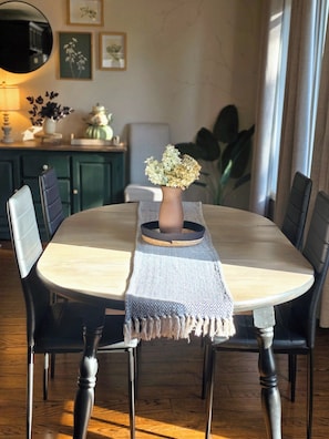 A dining table with a vase of flowers, a woven placemat, and black chairs. - ○Small Town Pearl○ 2Level Hidden Gem Near RedDeer│1K+2Q│Private Yard│Firepit+BBQ (Penhold)