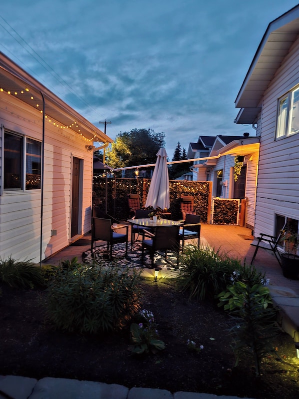 Eine Terrasse mit Gartenmöbeln, einem Sonnenschirm und Lichterketten.