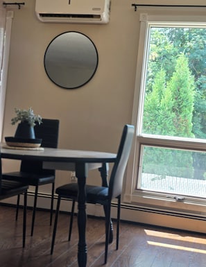 A dining area with a table, chairs, a potted plant, a round mirror, and a window with a view of greenery. - ○Small Town Pearl○ 2Level Hidden Gem Near RedDeer│1K+2Q│Private Yard│Firepit+BBQ (Penhold)