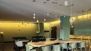 A modern dining area with a long communal table, multiple chairs, and hanging spherical light fixtures.