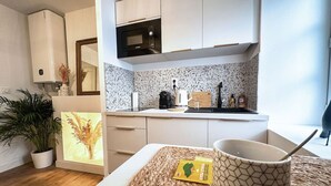 Una cocina moderna con armarios blancos, un microondas y un salpicadero moteado. Hay una planta, un cuadro enmarcado y una mesa con una taza y un paquete de tierra orgánica.
