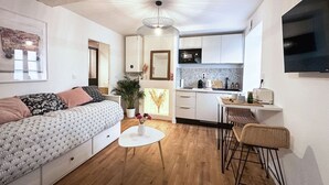 Un espacio habitable compacto con sofá, mesa de comedor, zona de cocina y lámpara de techo.