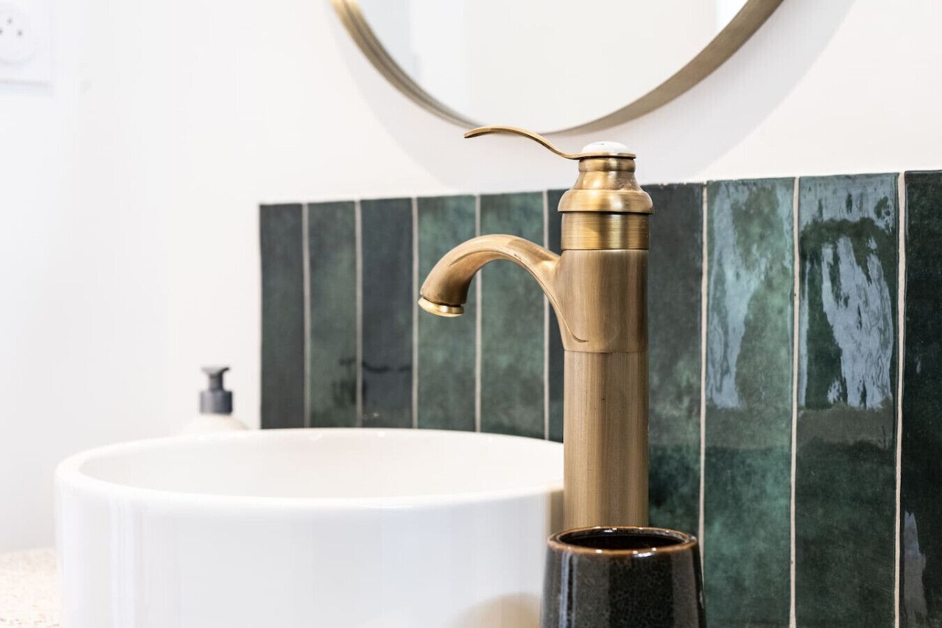 A bathroom with a white sink, a gold faucet, and green tiles.