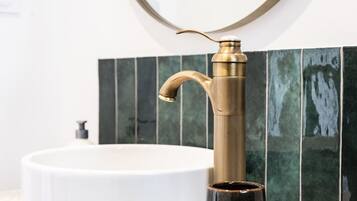A bathroom with a white sink, a gold faucet, and green tiles.
