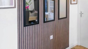 A hallway with vertical wooden paneling, two framed mirrors, and a door. - Le Réservoir - Quiet, residential apartment (Vichy)