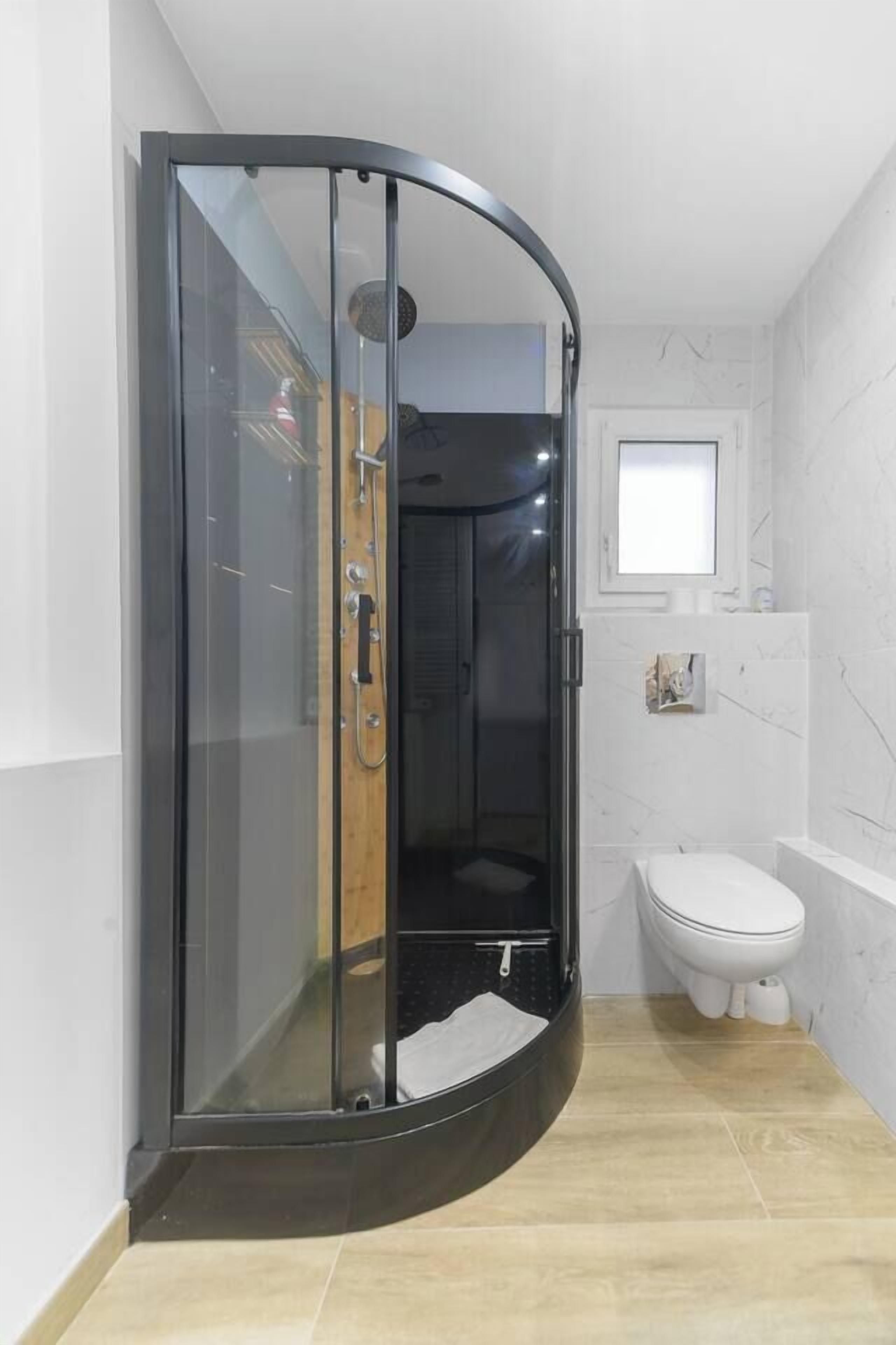 Ein modernes Badezimmer mit einer begehbaren Glasdusche, einer weißen Toilette und einer Badewanne.