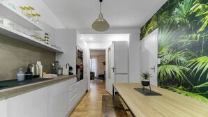 A modern kitchen with white cabinetry, a wooden dining table, and a large tropical plant mural. - Le Réservoir - Quiet, residential apartment (Vichy)