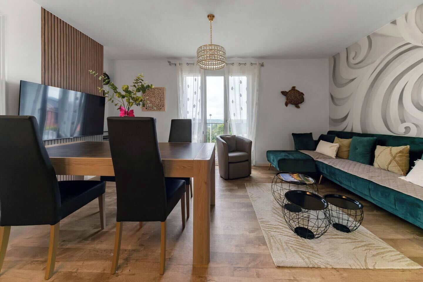 Una sala de estar moderna con una mesa de comedor de madera, sillas negras, un sofá verde y un televisor.