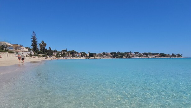 A beach with clear shallow waters, a sandy shore, and a distant town. - Shati Luxury- Private Heated Pool, sea view, two steps from beach (Fontane Bianche)
