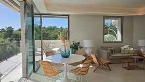 A modern living room with a glass balcony, wicker furniture, a white sofa, and a view of greenery. - Shati Luxury- Private Heated Pool, sea view, two steps from beach (Fontane Bianche)