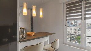 Una cocina moderna con refrigerador empotrado, una encimera con un hervidor y un tazón, tres lámparas colgantes y dos taburetes de bar.