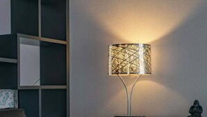 Una sala moderna con un sofá de cuero, un cojín estampado, una consola blanca y una lámpara de pared con diseño geométrico.