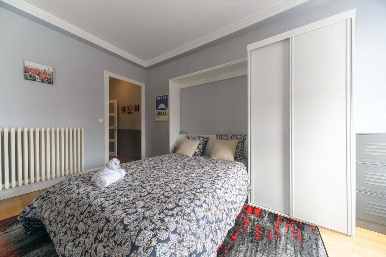 A bedroom with a bed, a radiator, a door, and a poster on the wall.