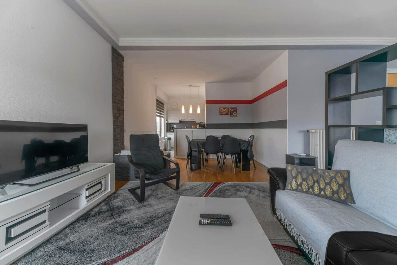 Uma sala de estar moderna com uma televisão de tela plana, um sofá, uma mesa de centro e uma área de jantar com cadeiras e uma mesa.