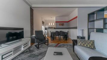 Uma sala de estar moderna com uma televisão de tela plana, um sofá, uma mesa de centro e uma área de jantar com cadeiras e uma mesa.