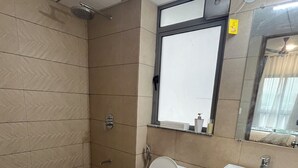 A bathroom with a toilet, sink, shower, and a mirror.