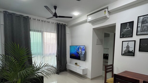 A modern living room with a flat-screen TV, ceiling fan, and dining area with chairs and a table.