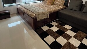 A bedroom with a bed, a sofa, a checkered rug, and a window with curtains.