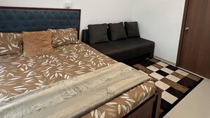 A bedroom with a bed, a sofa, a ceiling fan, and a door.