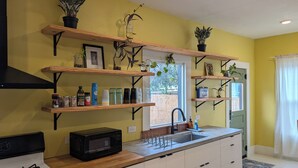 A kitchen with wooden shelves, a microwave, a gas stove, and a sink.