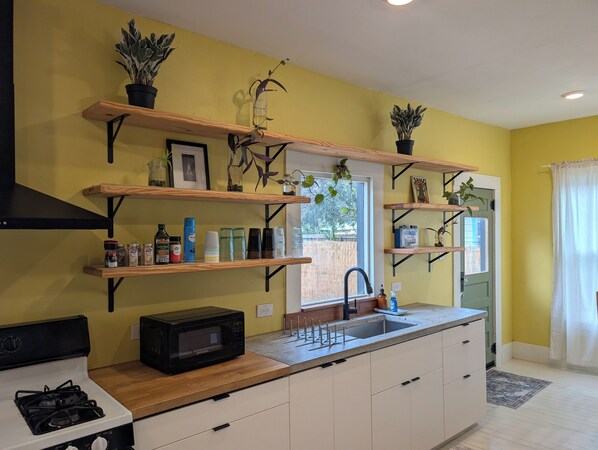 A kitchen with wooden shelves, a microwave, a gas stove, and a sink.