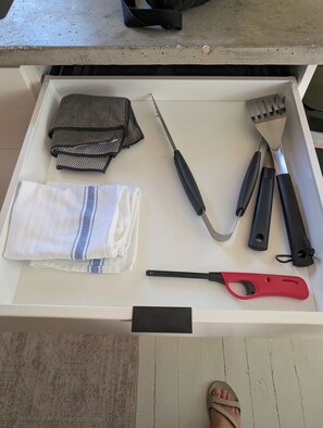 A drawer with kitchen utensils, a towel, and a pair of sandals.