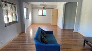Une pièce spacieuse avec un plancher en bois, un canapé bleu agrémenté de coussins à motifs et un projecteur fixé au plafond.