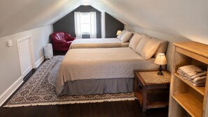 Ein Schlafzimmer mit zwei Betten, einem roten Sessel, einem Nachttisch mit Lampe und einem Regal mit Handtüchern.