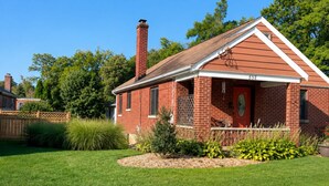 Ein rotes Ziegelhaus mit Schornstein, einer Veranda und einem gepflegten Rasen.