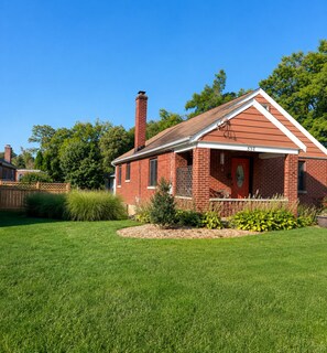 Une maison en briques rouges, dotée d’une cheminée, d’un porche et d’une pelouse bien entretenue.