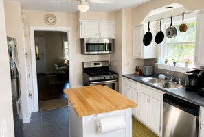 A kitchen with white cabinets, a wooden countertop, stainless steel appliances, and hanging pots. - Spacious Brick Home - Sleeps 8 - Near Downtown (Milford)