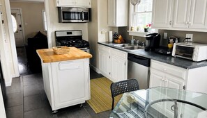 Une cuisine compacte avec des meubles blancs, un four à micro-ondes, une cuisinière, une machine à café et un grille-pain.