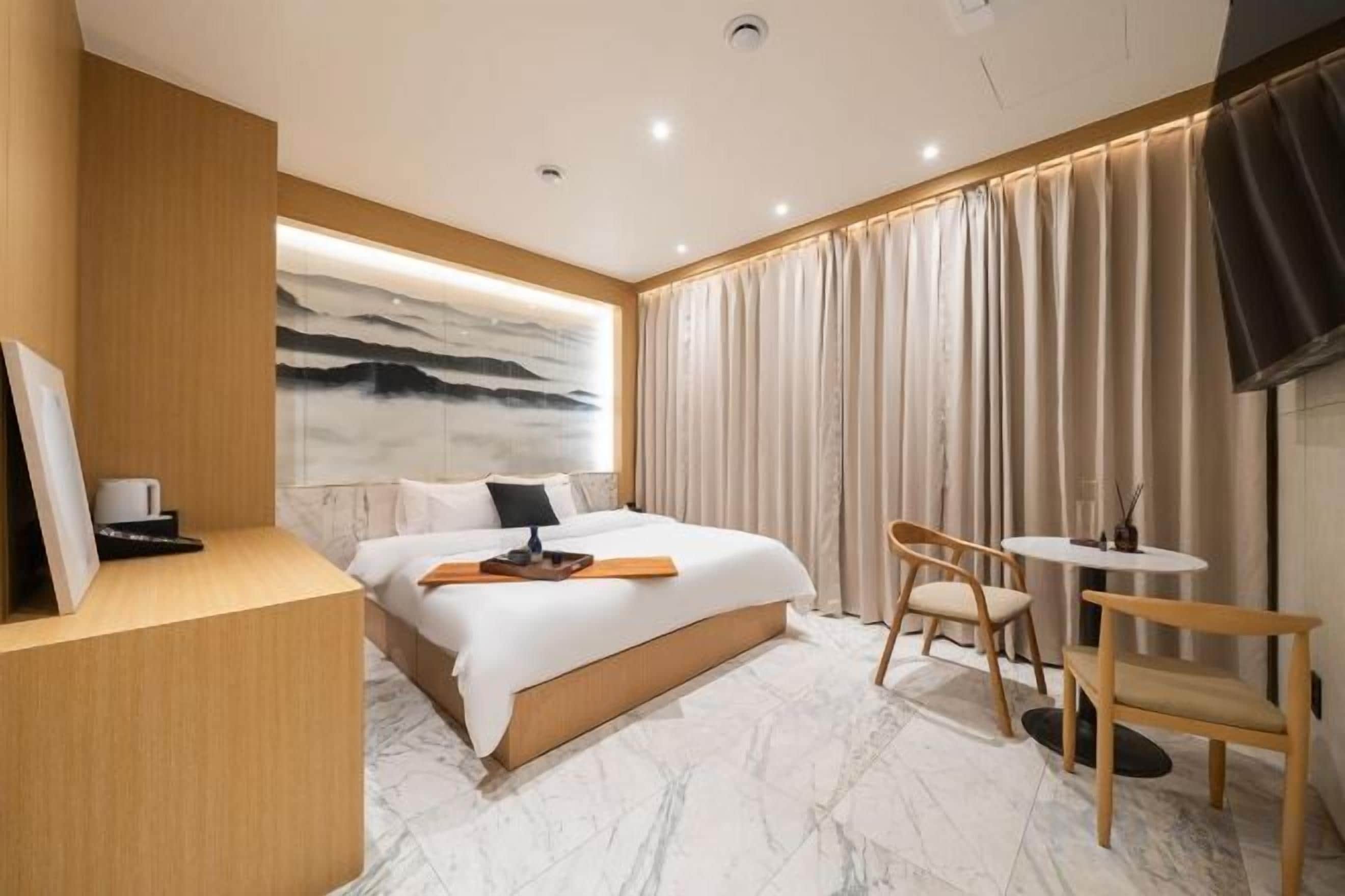 A hotel room with a bed, a desk, a chair, and a TV.