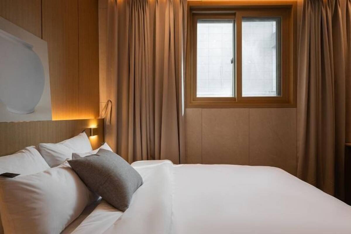 Una habitación de hotel con una cama, cortinas, una ventana y una lámpara de pared.