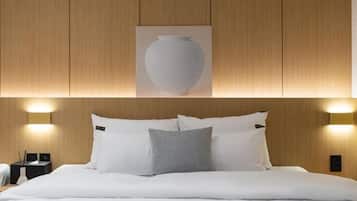 A hotel room with a bed, pillows, a wall-mounted light fixture, and a framed picture above the bed.