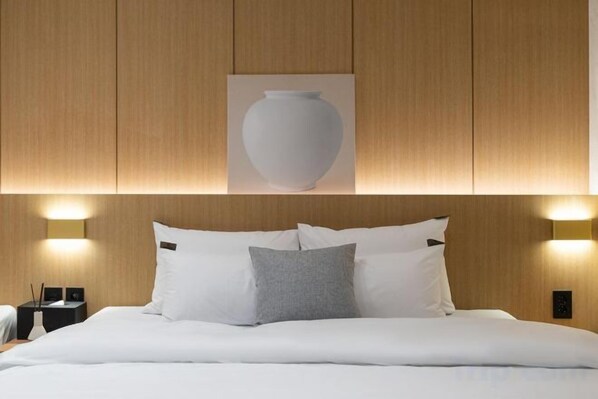 A hotel room with a bed, pillows, a wall-mounted light fixture, and a framed picture above the bed.