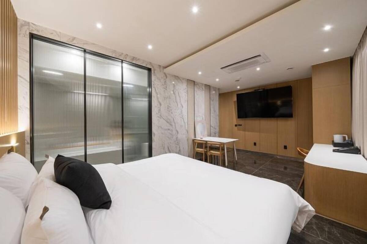 Una habitación de hotel moderna con una cama grande, un escritorio, una silla, un televisor y un ventanal corredero.