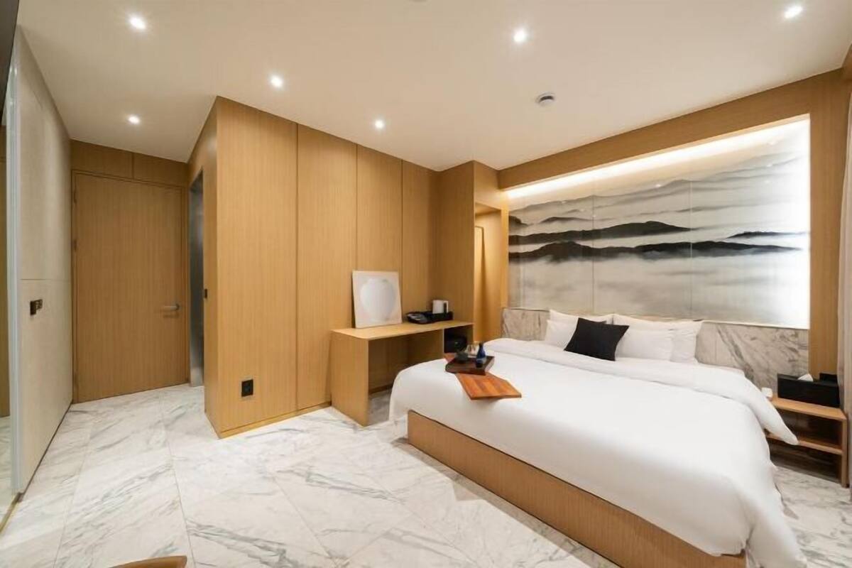 Un dormitorio moderno con una cama grande, paneles de madera, suelo de mármol y una obra de arte colgada en la pared.