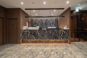 A reception desk with a marble top, wooden paneling on the walls, and a modern light fixture above. - Incheon BrownDot Hotel Guwol (Incheon)