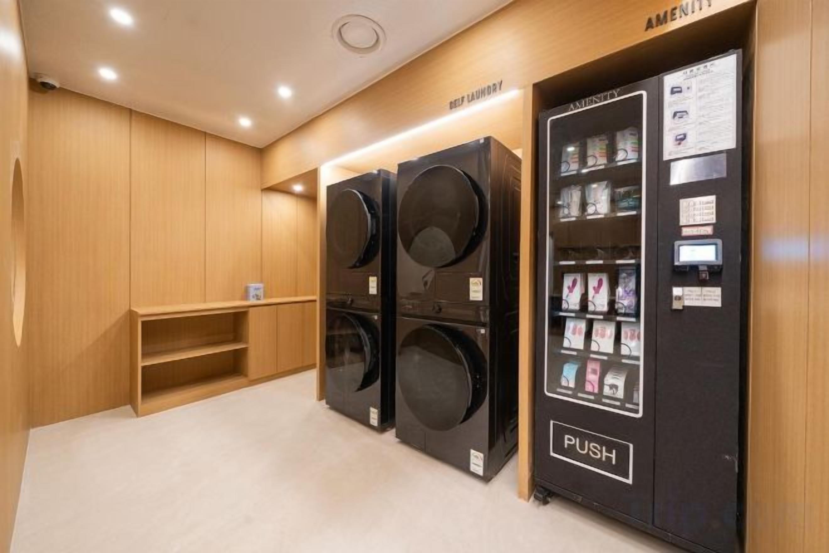 A laundry facility with two large washers and dryers, a vending machine, and a wooden bench.