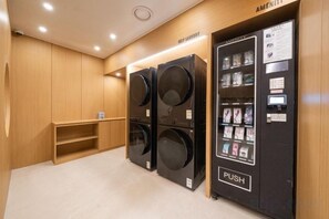 A laundry facility with two large washers and dryers, a vending machine, and a wooden bench. - Incheon BrownDot Hotel Guwol (Incheon)