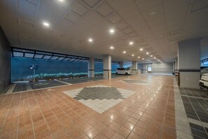 A spacious indoor parking area with a tiled floor, a white car parked, and a large window with a view of the sky. - Incheon BrownDot Hotel Guwol (Incheon)