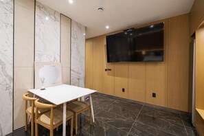 A modern room with a white table and wooden chairs, a flat-screen TV mounted on the wall, and marble-patterned walls.