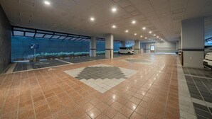 A spacious indoor parking area with a tiled floor, large windows, and a white car parked in the distance. - Incheon BrownDot Hotel Guwol (Incheon)