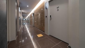 A modern hotel corridor with a shiny tiled floor, a wooden wall, and a door marked with the number 215. - Incheon BrownDot Hotel Guwol (Incheon)