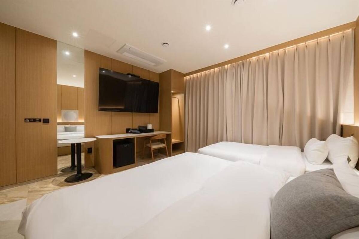 Habitación de hotel con dos camas, un escritorio, un televisor de pantalla plana y un ventanal con cortinas.