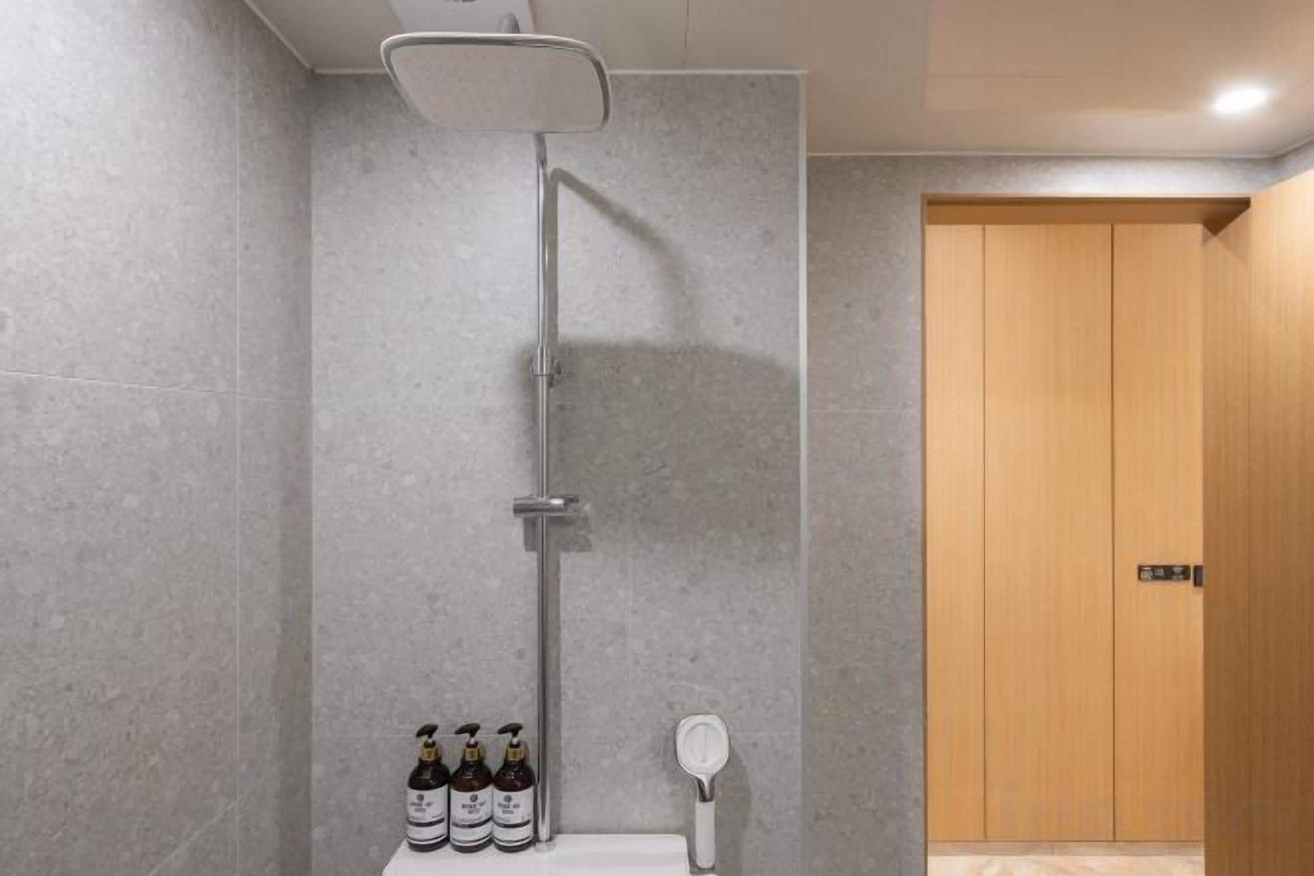 A shower with a handheld showerhead, a wall-mounted faucet, and a toilet with a soap dispenser.