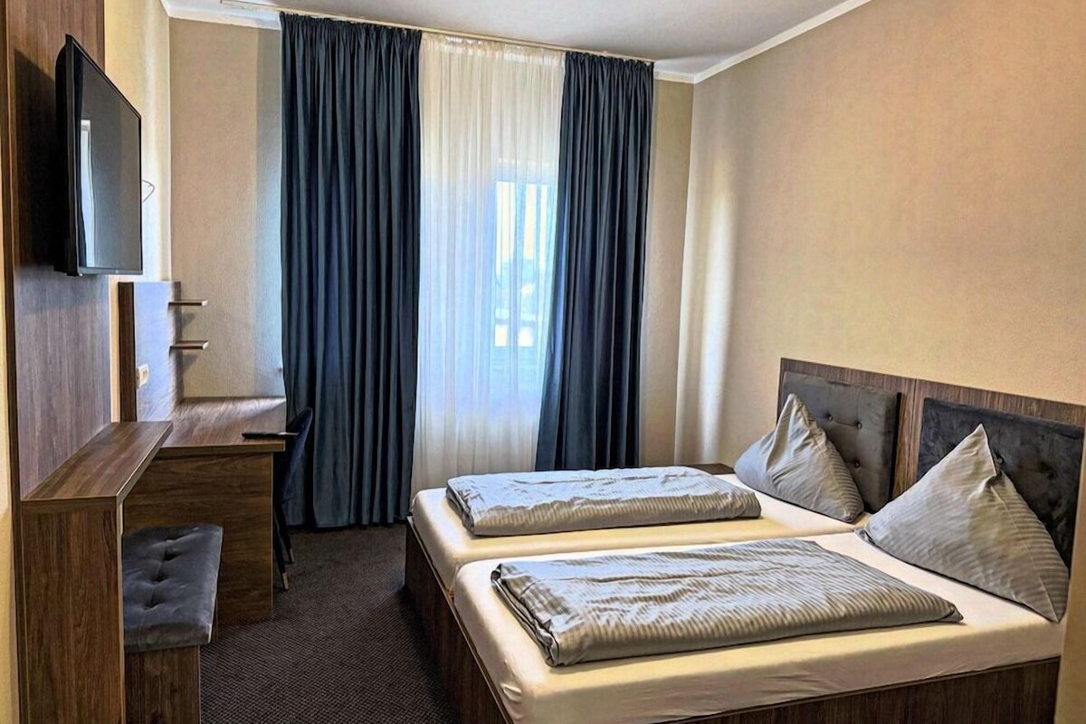 Habitació d'hotel amb un llit, escriptori, televisió i finestra amb cortines.